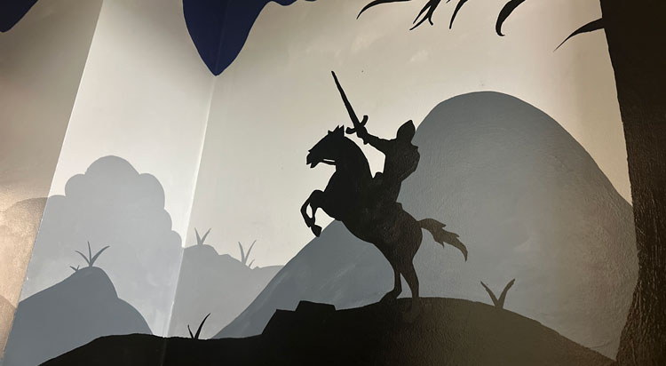 Silhouette painting on a wall of a Camelot knight charging on a horse with hills in the background.