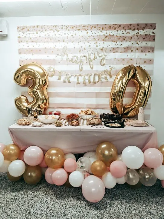 Happy Birthday decorated table, with Mylar balloons, pink and white striped banner, and various snacks on a table with a pink tablecloth.