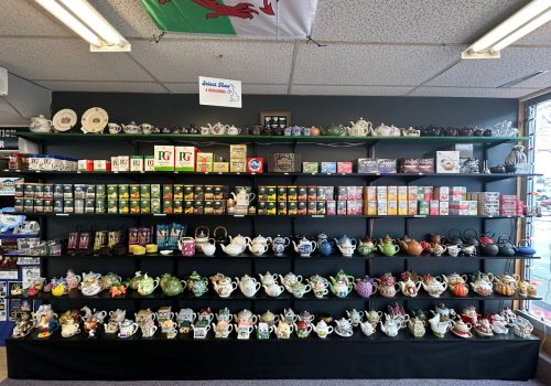 A black wall with black shelves with various unique teapots and tea sets as well as several different tins and boxes of teas from Britain.