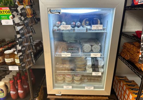 Small refrigerator with pudding, mac and cheese pies, bacon, crumpets, and other British food items.
