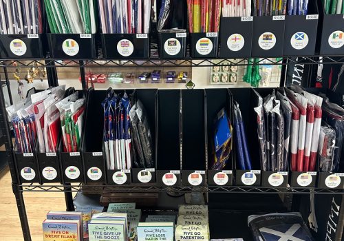 Shelves with flags of various origins from America to Europe as well as a pirate flag and a rainbow flag, as well as some books, a journal, and a blanket.